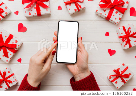 Woman hand holding mobile phone with blank screen on colored background with hearts, valentine day concept top view flat lay Woman hand holding mobile phone with blank screen on colored background with hearts, valentine day concept top view flat lay 136160282