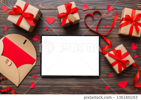 Top view of digital tablet with gift boxes and hearts on colorful background. Tablet with black screen with Holiday decorations gift box top view 136160283