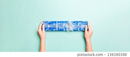 Woman hands give wrapped christmas or other holiday handmade present in colored paper. Present box, decoration of gift on Blue table, top view with copy space Woman hands give wrapped christmas or other holiday handmade present in colored paper. Present box, decoration of gift on Blue table, top view with copy space 136160380