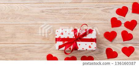 Valentine or other holiday handmade present in paper with red hearts and gifts box in holiday wrapper. Present box of gift on orange wooden table top view with copy space, empty space for design 136160387