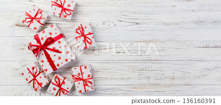 Valentine or other holiday handmade present in paper with red hearts and gifts box in holiday wrapper. Present box of gift on white wooden table top view with copy space, empty space for design 136160391