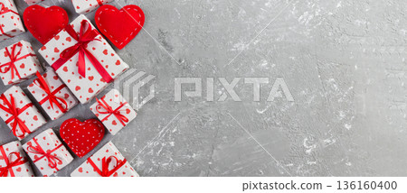 Valentine or other holiday handmade present in paper with red hearts and gifts box in holiday wrapper. Present box of gift on grey cement table top view with copy space, empty space for design Valentine or other holiday handmade present in paper with red hearts and gifts box in holiday wrapper. Present box of gift on grey cement table top view with copy space, empty space for design 136160400