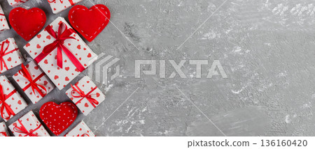 Valentine or other holiday handmade present in paper with red hearts and gifts box in holiday wrapper. Present box of gift on grey cement table top view with copy space, empty space for design 136160420