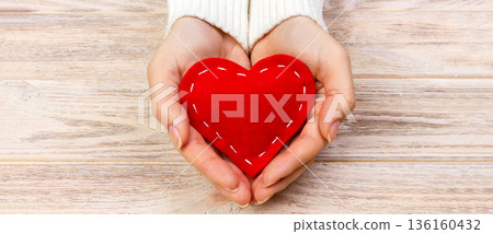red heart in hands closeup on wooden background 136160432