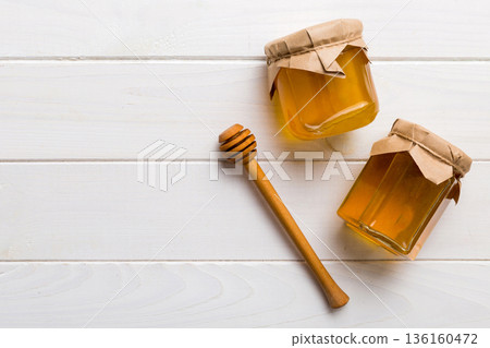 Glass jar of honey with wooden drizzler on colored background. Honey pot and dipper high above. Top view copy space 136160472