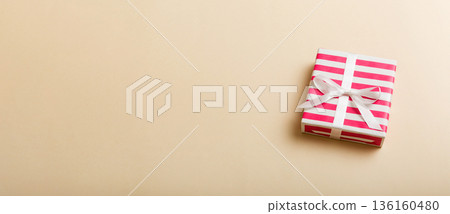 wrapped Christmas or other holiday handmade gift box in color paper with ribbon on colored background. Present box, decoration of gift on colored table, top view with copy space 136160480