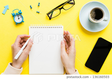 Woman hand with pencil writing on notebook and hold coffee cup. Woman working on office table with coffee Woman hand with pencil writing on notebook and hold coffee cup. Woman working on office table with coffee 136160503