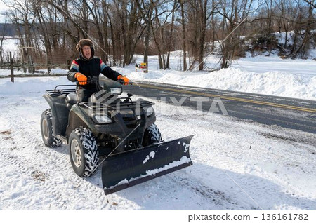 Senior man in fur hat and snowsuit plows huge snow with ATV rural landscape 136161782