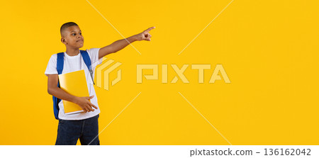 Preteen black boy pointing aside at copy space confidently while holding notebook 136162042