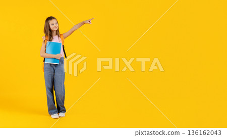 Preteen schoolgirl pointing at copy space while holding notebook on yellow background Preteen schoolgirl pointing at copy space while holding notebook on yellow background 136162043