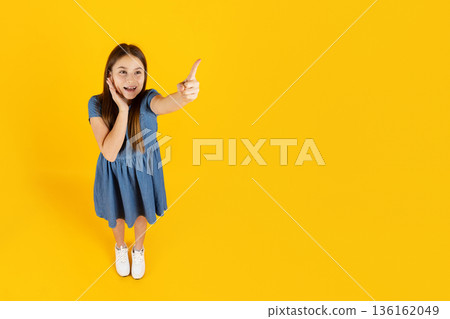 Surprised preteen girl points forward with excitement, expressing discovery and curiosity 136162049