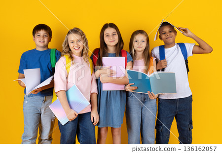 Portrait of preteen pupils holding books and notebooks on yellow studio background Portrait of preteen pupils holding books and notebooks on yellow studio background 136162057