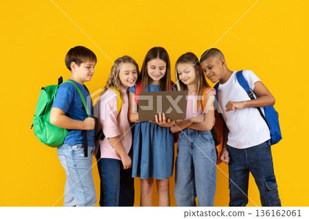 Preteen pupils using laptop together on yellow studio background Preteen pupils using laptop together on yellow studio background 136162061