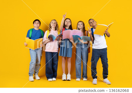 Preteen children looking up with books in hands on yellow studio background Preteen children looking up with books in hands on yellow studio background 136162068