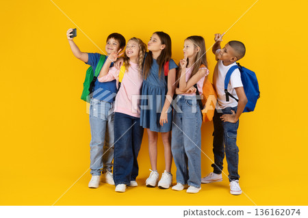 Preteen children taking selfie together on yellow studio background 136162074