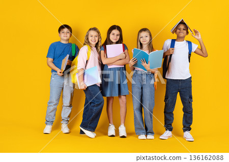 Group of preteen children posing with notebooks and backpacks on yellow background 136162088