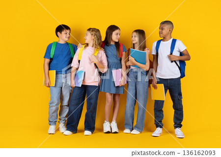 Preteen pupils interacting and talking together while holding notebooks on yellow background 136162093