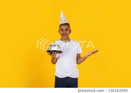 Black preteen boy holding birthday cake on yellow studio background Black preteen boy holding birthday cake on yellow studio background 136162095