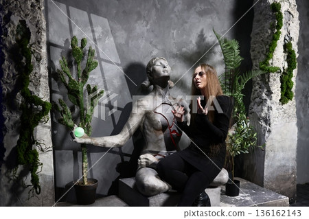Graceful woman seated near sculpture and vibrant foliage 136162143