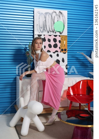 Individual dressed in pink skirt sitting on white sofa against blue wall Individual dressed in pink skirt sitting on white sofa against blue wall 136162145