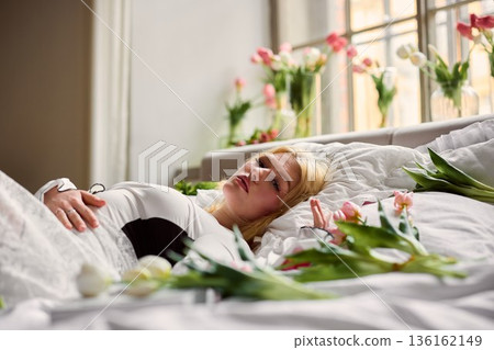 Serene woman resting, Serene female lying peacefully beside window with blooming tulips and cozy bedding setup Serene woman resting, Serene female lying peacefully beside window with blooming tulips and cozy bedding setup 136162149