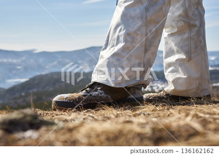 Man standing with snow covered boots and pants on dry grass outdoors. Hiking and winter outdoor activity concept for adventurer. 136162162