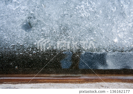 Frozen window with ice and air bubbles close up for winter background and cold weather concept with icy texture detail Frozen window with ice and air bubbles close up for winter background and cold weather concept with icy texture detail 136162177