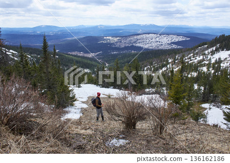 Hiker watching scenic mountain landscape with forest and snow. Adventure travel in wild nature exploring during cold season. Mount Argydzhek 136162186