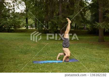 Individual executing handstand on blue mat in park environment Individual executing handstand on blue mat in park environment 136162192