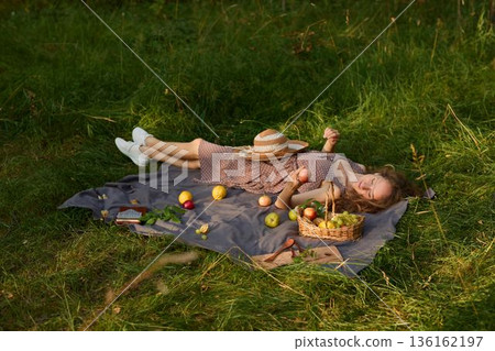Relaxed woman lying on grass with basket and apples present Relaxed woman lying on grass with basket and apples present 136162197