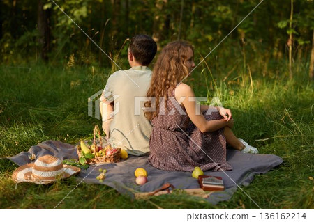 Pair resting back to back beneath trees with picnic and sunset glow Pair resting back to back beneath trees with picnic and sunset glow 136162214