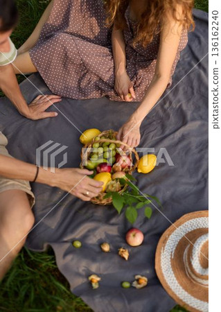 Romantic pair seated on blanket exchanging fruits and conversation outside 136162240