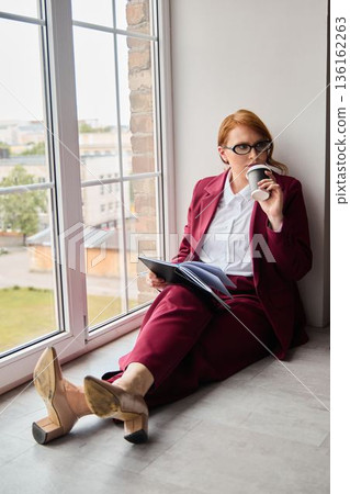 Elegant woman in burgundy attire enjoys city view and studies Elegant woman in burgundy attire enjoys city view and studies 136162263