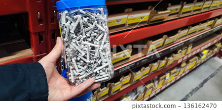 A man's hand picking up a handful of metal nails from a cardboard box at a hardware store or warehouse. Concept art of handicrafts, building materials, craftsmanship, and industrial supplies. 136162470