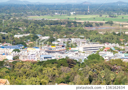 High angle view of a small town nestled in a lush tropical landscape with green trees, residential houses, and distant mountains. Scenic aerial shot of rural urban development in Southeast Asia. 136162634