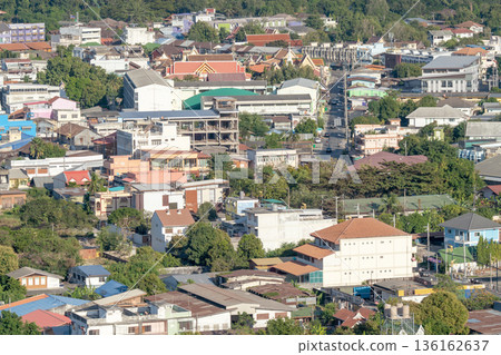 Aerial view of a dense urban landscape in Thailand featuring colorful rooftops, traditional temples, and lush green trees. A vibrant cityscape showcasing local architecture and residential areas. Aerial view of a dense urban landscape in Thailand featuring colorful rooftops, traditional temples, and lush green trees. A vibrant cityscape showcasing local architecture and residential areas. 136162637