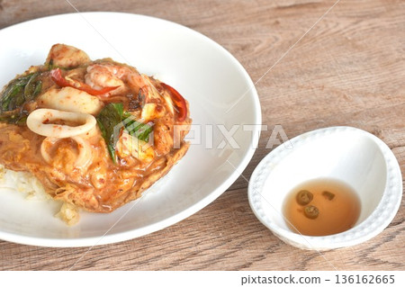 Thai steamed red Curry with seafood on cream egg omelet topping plain rice in plate Thai steamed red Curry with seafood on cream egg omelet topping plain rice in plate 136162665