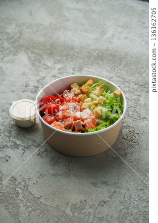 Fresh salad with vegetables and dressing in a container on a gray surface 136162705
