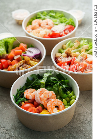 Fresh salads with shrimp and vegetables served in bowls on a stone surface 136162712