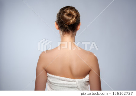 Woman stands with back turned, towel wrapped, in simple indoor setting with plain background 136162727