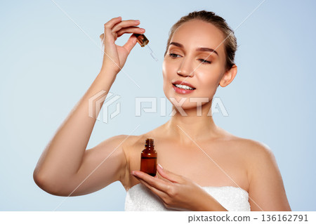 Woman holding dropper bottle with liquid near her face during skincare routine Woman holding dropper bottle with liquid near her face during skincare routine 136162791