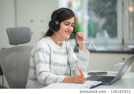 Young woman working remotely using laptop and headset Young woman working remotely using laptop and headset 136162831