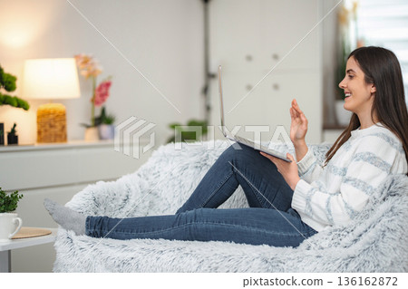 Woman waving hello on video call using laptop at home Woman waving hello on video call using laptop at home 136162872