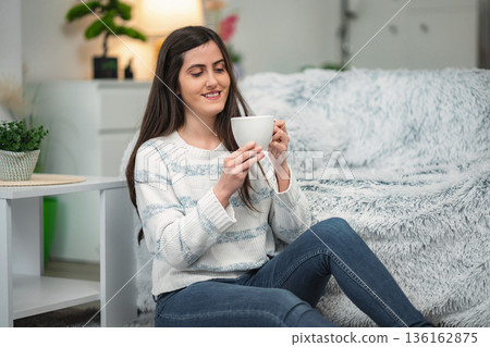 Woman enjoying hot drink sitting on floor at home Woman enjoying hot drink sitting on floor at home 136162875