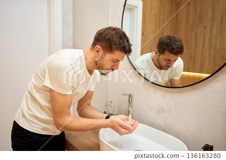 Man standing in bathroom and washing hands under running water at sink Man standing in bathroom and washing hands under running water at sink 136163280