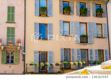 Windows with green wooden shutters. Flowers in pot on balcony. Italy summer day. Italian style facade street. Windows with green wooden shutters. Flowers in pot on balcony. Italy summer day. Italian style facade street. 136163597