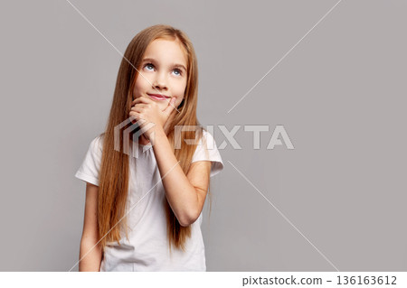Beautiful thoughtful young girl with long hair looking up, isolated on gray studio background, expressing curiosity, imagination and creative childhood thinking in beauty child portrait 136163612