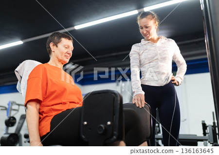 Older woman training legs with personal instructor in gym 136163645