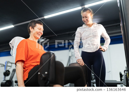 Personal trainer assisting senior woman with leg exercises 136163646