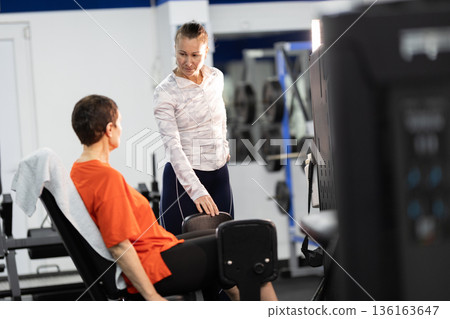 Personal trainer guiding woman on leg exercise machine 136163647